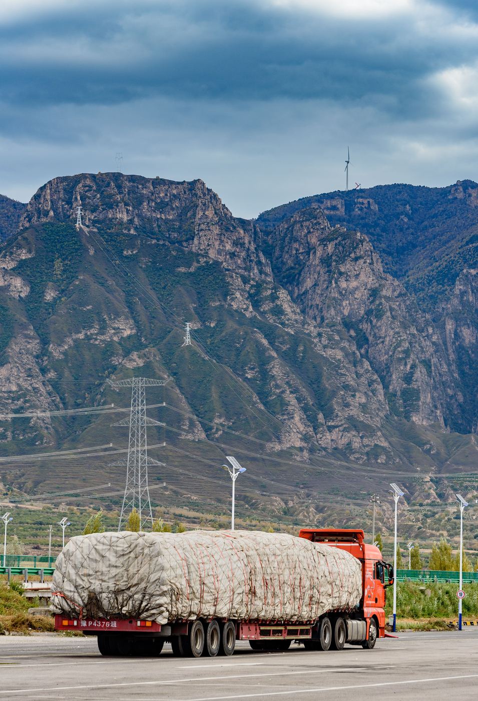 Heavy truck beneath power transmission pylons and mountains